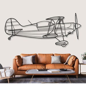 Puede incluir: Arte mural de metal negro de un biplano. El biplano presenta un contorno detallado de la estructura de la aeronave, incluyendo las alas, el fuselaje y la hélice. La obra de arte está montada en una pared de color neutro.