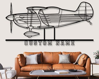 May include: Black metal airplane wall art with a propeller and the text "CUSTOM NAME" below. The artwork is displayed above a brown leather sofa with pillows and a coffee table.