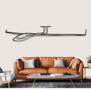 May include: A black metal wall art piece depicting a glider airplane. The artwork is a line drawing style, showing the glider's wings, fuselage, and tail. The art is mounted on a light-colored wall above a brown leather sofa.