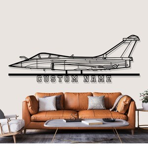 Pode incluir: Arte de parede em metal preto com um contorno detalhado de um avião de combate. O texto "CUSTOM NAME" é exibido abaixo do avião. Esta peça decorativa é projetada para montagem na parede.