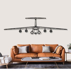 May include: Black metal airplane wall art. The artwork depicts a detailed outline of a large aircraft, including wings, fuselage, and landing gear. The plane is mounted on a neutral-colored wall above a brown leather sofa.