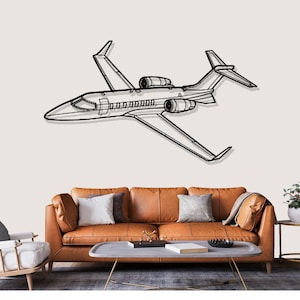 May include: A black and white metal wall art piece depicting a detailed airplane. The artwork features the outline of a jet with wings, engines, and a cockpit. The plane is mounted on a neutral-colored wall above a brown leather sofa.