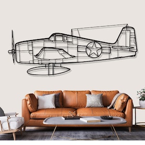 May include: Black metal airplane wall art. The artwork depicts a vintage airplane with a propeller, wings, and a star emblem. The art piece is mounted on a light-colored wall above a brown leather sofa, adding a touch of aviation history to the room.