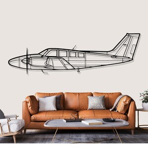 May include: Black metal airplane wall art. The outline of a small aircraft with a propeller is mounted on a wall. The artwork is above a brown leather sofa with pillows and a coffee table.