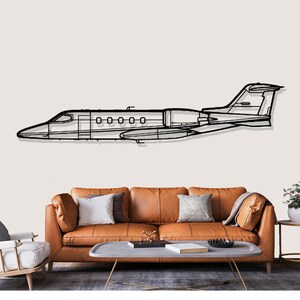 May include: Black metal wall art depicting a detailed outline of a jet airplane. The artwork features the plane's fuselage, wings, and tail, with visible windows and engine details. The art piece is mounted on a neutral-colored wall above a brown leather sofa.