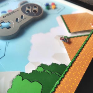 Expositor enmarcado con mando de Super Nintendo y Mario World: arte mural de videojuegos retro