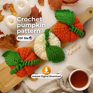 Peut inclure: Trois citrouilles crochetées orange et crème avec des feuilles vertes sont posées sur une planche en bois. L'image comprend le texte "Crochet pumpkin pattern" et "PDF file". Une tasse de thé et des bougies sont également dans l'image. Les mots "+ Video Tutorial" et "Instant Digital Download" sont également visibles.