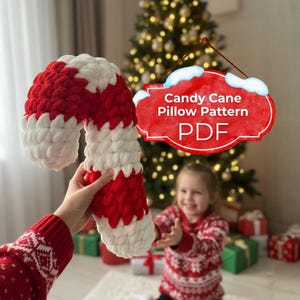 Puede incluir: Una almohada grande, hecha a mano, con forma de bastón de caramelo a rayas rojas y blancas. La almohada se sostiene frente a un árbol de Navidad. Un letrero dice "Candy Cane Pillow Pattern PDF".