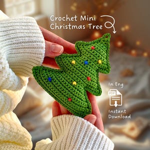 Op de afbeelding: Een groene gehaakte kerstboom met kleurrijke decoratieve accenten wordt in de handen van een persoon gehouden. De boom heeft de vorm van een klassieke kerstboom en heeft kleine, kleurrijke stippen. Tekst op de afbeelding luidt "Crochet Mini Christmas Tree" en "Instant Download".