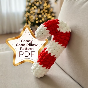 Peut inclure: Un oreiller en forme de canne en sucre rouge et blanc, en matière douce et texturée, est posé sur un canapé clair. Un graphisme en forme d'étoile dorée avec le texte "Candy Cane Pillow Pattern PDF" est suspendu au premier plan. Un sapin de Noël avec des lumières floues est en arrière-plan.