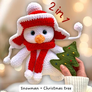 Puede incluir: Un muñeco de nieve blanco tejido a ganchillo con un gorro y bufanda rojos, sosteniendo un árbol de Navidad tejido a ganchillo verde. El muñeco de nieve tiene ojos azules y una nariz naranja. El texto "2 en 1" es visible. El texto "Muñeco de nieve + árbol de Navidad" también es visible.