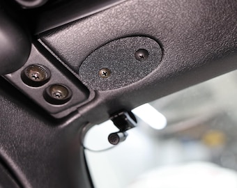 May include: Close-up of a black car interior, focusing on the roof lining. Visible are screws, a small oval-shaped panel, and a microphone. The textured surface and hardware details suggest a functional design.