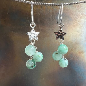 May include: Silver star earrings with three green gemstone beads dangling from each star.