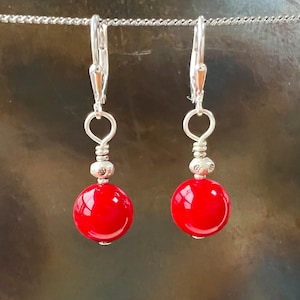 May include: A pair of silver dangle earrings with red round beads. The earrings have a hook closure.