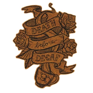 Puede incluir: Un posavasos de corcho marrón con una ilustración en blanco y negro de una taza de café con una calavera y huesos cruzados, rosas y una pancarta que dice "Death before Decaf".