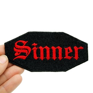May include: Black iron-on patch with red embroidered text that reads "Sinner" in a gothic font.