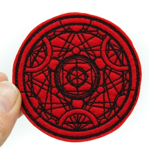 May include: Red felt circle with a black embroidered geometric design. The design is a complex pattern of circles, lines, and dots.