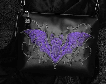 May include: Black shoulder bag featuring a purple embroidered bat motif. The bag has an adjustable strap and a zip closure. The bat design is centrally placed on the front, with detailed wing patterns.