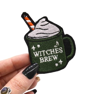 May include: Embroidered patch featuring a green mug with the words "Witches Brew" in white. The mug has a white whipped cream topping and a straw with orange and white stripes. The patch is held against a white background.