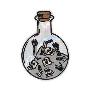 May include: A clear glass bottle with a cork stopper filled with a pile of white skulls and bones. The bottle has a glittery iridescent finish.