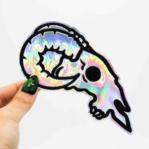 May include: A black and white outline of a ram skull with iridescent holographic backing.