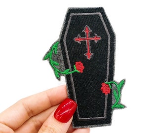 May include: Black embroidered coffin with a red cross and two red roses with green stems. The coffin is surrounded by a gray border.