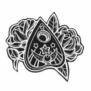May include: Black and white illustration of a Ouija board planchette with a crescent moon and stars, surrounded by stylized flowers.