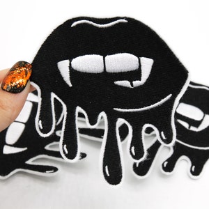 May include: Three black iron-on patches featuring dripping black lips and white fangs. The patches are embroidered with white thread.