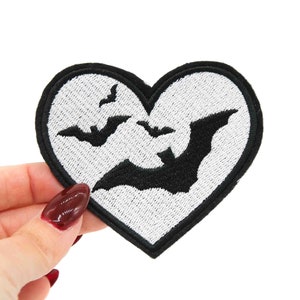 Puede incluir: Parche blanco en forma de corazón con murciélagos bordados en negro.