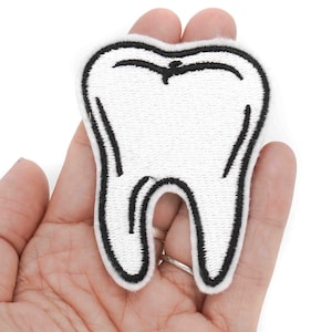 May include: White embroidered tooth patch with black outline. The patch is held in a hand.