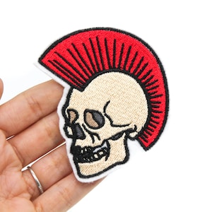 May include: Embroidered iron-on patch featuring a white skull with a red mohawk. The skull has black eyes and a black mouth.