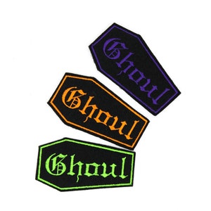 May include: Three black coffin-shaped patches with the word "Ghoul" embroidered in orange, green, and purple.