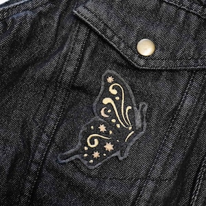 May include: A black denim jacket with a gold embroidered butterfly patch on the pocket.