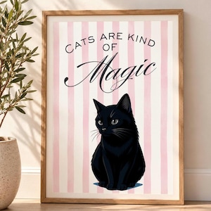 May include: A framed wall art print featuring a black cat illustration centered on a background of vertical light pink and white stripes. The text "CATS ARE KIND OF Magic" is printed in black above the cat in a mix of sans-serif and script fonts.