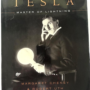 May include: A hardcover book titled Tesla: Master of Lightning by Margaret Cheney and Robert Uth. The black cover features a black and white portrait of Nikola Tesla holding a glowing circular light source, with gold lettering for the title.
