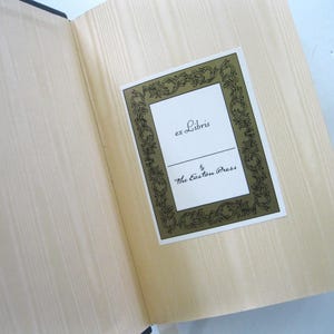 Pode incluir: Livro aberto com p&aacute;ginas claras e uma etiqueta decorativa. A etiqueta, emoldurada em dourado, diz "ex Libris" e "The Easton Press" em uma escrita elegante. As p&aacute;ginas do livro t&ecirc;m uma sutil textura de gr&atilde;o de madeira.