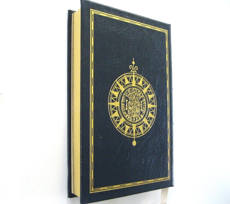 Pode incluir: Um livro de capa dura azul marinho com detalhes dourados. A capa apresenta um emblema dourado com um design de b&uacute;ssola. As p&aacute;ginas do livro t&ecirc;m bordas douradas. Uma fita branca como marcador de livro &eacute; vis&iacute;vel.