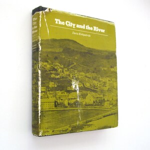 May include: A vintage book titled "The City and the River" by Doris Kirkpatrick. The cover is a faded olive green with a landscape illustration of a town and river. The book shows signs of wear.