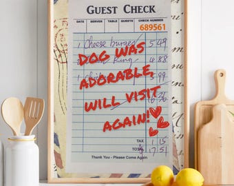 May include: A framed "Guest Check" print with handwritten text and red accents. The text includes "Dog Was Adorable" and "Will Visit Again!" with heart illustrations. The print is displayed on a kitchen counter with other decorative items.