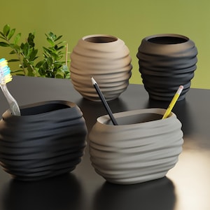 May include: Four oval-shaped containers with a horizontal ribbed texture. Two are black and two are beige. One black container holds a toothbrush, while the other holds a black pencil. One beige container holds a yellow pencil. The items are arranged in a group.