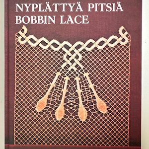 May include: A book cover with the title "NYPLÄTTYÄ PITSIÄ BOBBIN LACE" in white letters. The cover features a detailed illustration of bobbin lace in shades of beige and orange against a dark burgundy background. The author's name, EEVA-LIISA KORTELAHTI, is at the top.