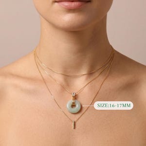 K&ouml;nnte beinhalten: Ein goldfarbenes Halsketten-Set mit drei Schichten. Die oberste Schicht ist eine feine Kette, die mittlere Schicht hat einen hellgr&uuml;nen Jade-Donut-Anh&auml;nger und die untere Schicht einen kleinen Stab-Anh&auml;nger. Gr&ouml;&szlig;e: 16-17mm.