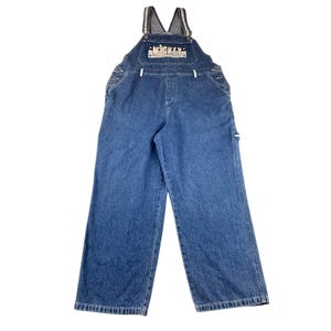 May include: Blue denim overalls with adjustable straps and a bib pocket. The bib features the word "MCGKEY" in a white and black design. The overalls have multiple pockets and a relaxed fit.