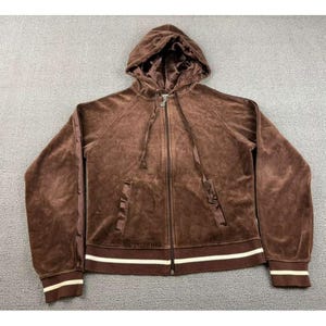 Op de afbeelding: Een bruine velours hoodie met ritssluiting, capuchon met trekkoord en twee voorzakken. De manchetten en zoom hebben witte strepen. De jas is gemaakt van een zacht, pluche materiaal.
