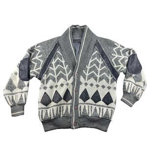 Könnte beinhalten: Eine weiße Keramik-Tasse mit schwarzem Henkel und dem Text "But First, Coffee" in schwarzer, handschriftlicher Schrift. Die Tasse steht auf einer weißen Oberfläche.