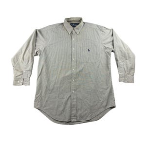 Puede incluir: Camisa de manga larga con estampado de rayas grises y blancas. La camisa tiene cuello abotonado, bolsillo en el pecho y un pequeño logotipo azul marino. Los puños tienen cierres de botón. Una prenda clásica.