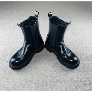 May include: A pair of black Chelsea boots with a glossy finish. The boots have elastic side panels and pull tabs at the back. The soles are thick and lugged.