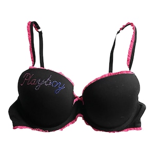 May include: Black bra with pink trim and straps. The bra features the word "Playboy" in rhinestones across the left cup. The bra has a classic silhouette with underwire support and adjustable straps.