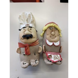 Può includere: Due figure di stoffa: uno chef e una donna. Lo chef indossa un cappello bianco, una sciarpa rossa e dei baffi neri. La donna ha capelli biondi di lana, una fascia rossa e un grembiule bianco con la scritta "Simpico". Entrambi hanno corpi beige.