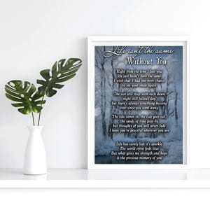 May include: A framed print with the text "Life isn't the same Without You" and a poem. The print is in a white frame and is displayed on a white surface. A white vase with green leaves is to the left.